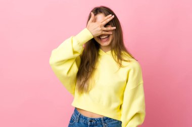 Soyutlanmış pembe arka planda genç bir kadın. Gözleri elleriyle kaplıyor ve gülümsüyor.