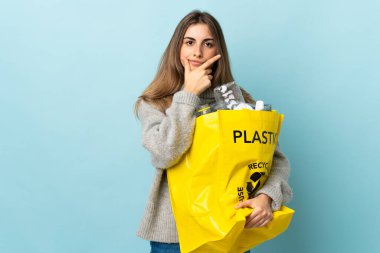 Bir çanta dolusu plastik şişeyi izole edilmiş mavinin üzerinde geri dönüştürmek için bir fikir tutarak.
