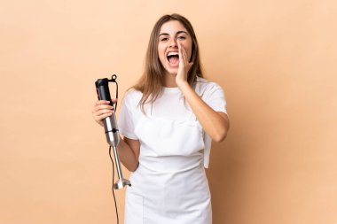 Arka planda el blenderi kullanan bir kadın bağırıyor ve bir şey duyuruyor.