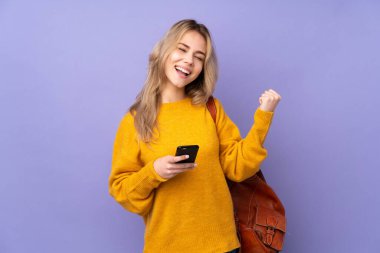 Mor arka planda izole edilmiş genç Rus öğrenci telefonu zafer pozisyonunda.