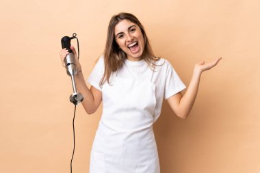 El blenderi kullanan bir kadın şok olmuş yüz ifadesi ile izole edilmiş bir arkaplanda