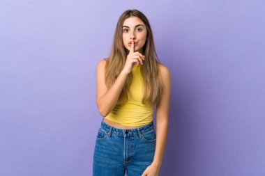 İzole edilmiş mor arka planda genç bir kadın sessizlik işareti gösteriyor. Parmağını ağzına sok.