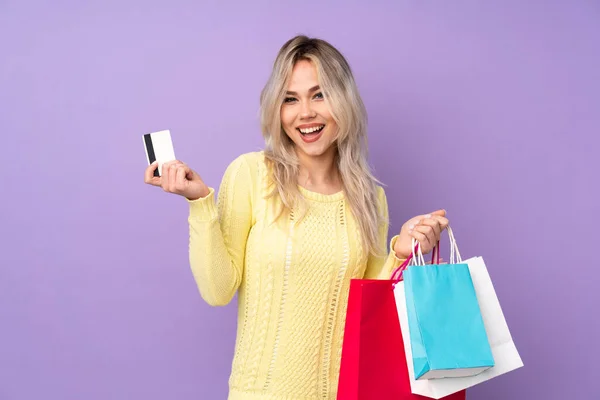 ティーンブロンド女の子上の隔離された紫背景保持ショッピングバッグとクレジットカード — ストック写真