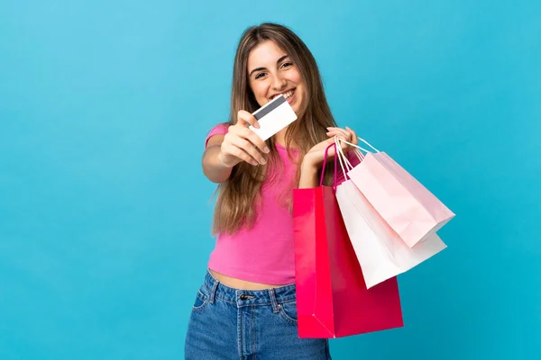 隔離された青の背景の上の若い女性ショッピングバッグとクレジットカードを保持 — ストック写真
