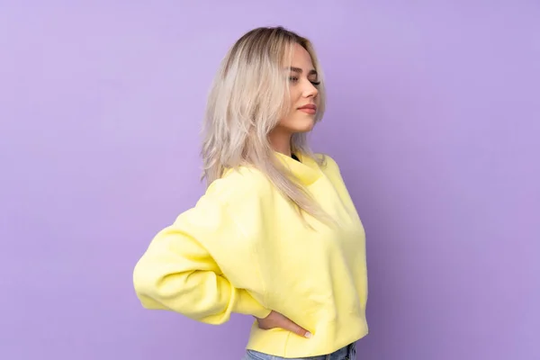 Teenager girl wearing a yellow sweatshirt over isolated purple background suffering from backache for having made an effort