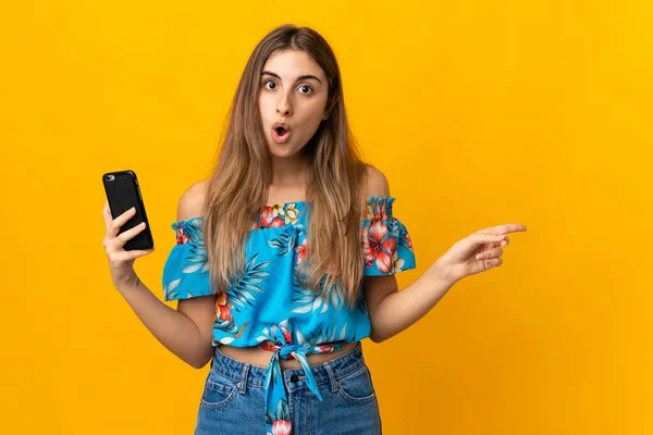 Jovem Mulher Usando Telefone Celular Sobre Fundo Amarelo Isolado Surpreendido — Fotografia de Stock