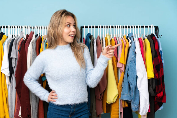 Teenager Russian girl buying some clothes isolated on blue background pointing finger to the side and presenting a product