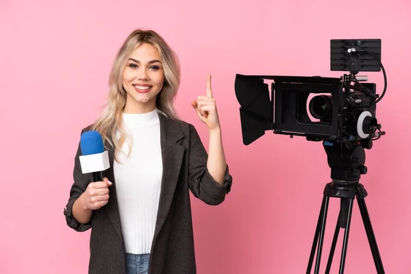 记者妇女手持话筒 在孤立的粉色背景上报道新闻 展示并举起一个手指表示最好的标志 — 图库照片