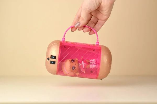 手はテーブルの上にプラスチックロール人形とピンクの容器を保持しています。Mga Entertainment Inc.が製造するLol Surpriseシリーズのおもちゃ. — ストック写真
