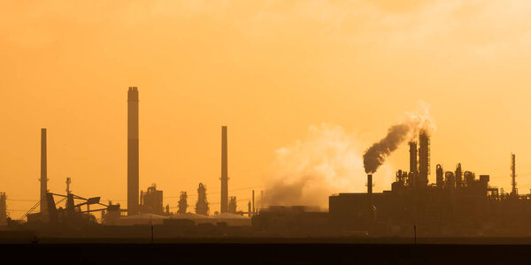 Dutch industrial plant with chimneys and windmill during sunset in Europoort, Rotterdam harbor