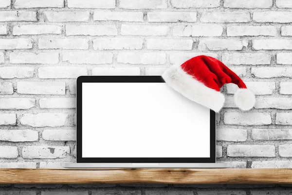 Computer portatile a schermo bianco su parete di mattoni bianchi con cappello di Natale — Foto Stock