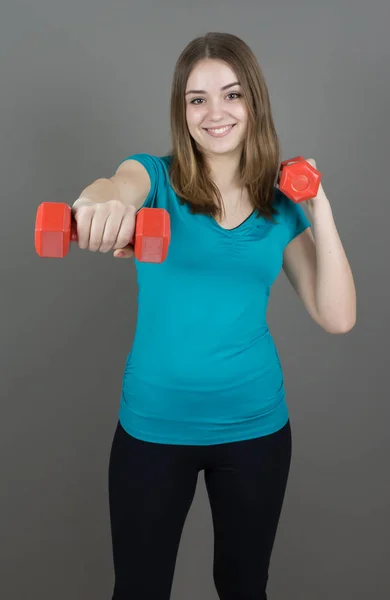 Dívka s dumpbells na šedém pozadí sport koncept posilovny — Stock fotografie