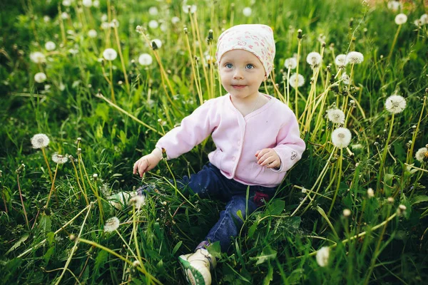 Little baby girl walking in the garden. Dandelions. Green grass. — Stock Photo, Image