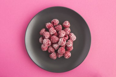 Pembe arka planda, siyah tabakta donmuş ahududu. Üst manzara. Boşluğu kopyala.