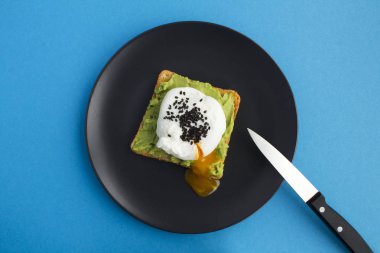 Haşlanmış yumurtalı sandviç ve mavi arka plandaki siyah tabakta avokado. Üst Manzara. Boşluğu kopyala.