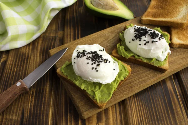 Sandwiches with poached eggs and avocado on the cutting board on the brown wooden background