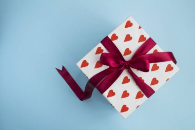 Kırmızı fiyonklu bir hediye ve mavi arka planda küçük kırmızı kalpler. Üst Manzara. Boşluğu kopyala.