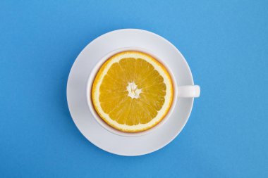 Mavi arka planda taze portakallı beyaz çay fincanı. Üst Manzara. Uzayı kopyala Yaratıcı gıda kolajı.