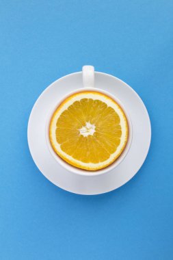 Mavi arka planda taze portakallı beyaz çay fincanı. Üst Manzara. Uzayı kopyala Yaratıcı gıda kolajı. Konum dikey.