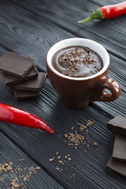 Kahverengi bardakta sıcak çikolata ve siyah ahşap arka planda kırmızı biber. Konum dikey.