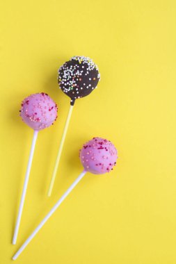 Sarı arka planda pembe ve çikolata kaplı kek çubukları. Üst Manzara. Uzayı kopyala Konum dikey.
