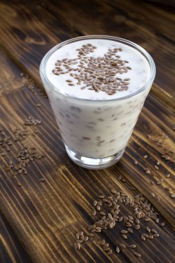 Yoğurt ya da kefir. Kahverengi ahşap arka plandaki bardakta keten tohumu var. Konum dikey. Boşluğu kopyala.