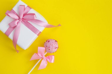 Sarı arka planda pembe kurdeleli hediye ve kek. Üst Manzara. Uzayı kopyala Yakın çekim..