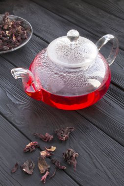 Siyah ahşap arka plandaki cam çaydanlıkta Hibiscus ya da Karkade çayı. Konum dikey. Yakın çekim..