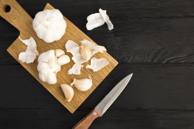 Siyah ahşap arka plandaki kahverengi kesme tahtasındaki kuru sarımsak. Üst Manzara. Boşluğu kopyala.