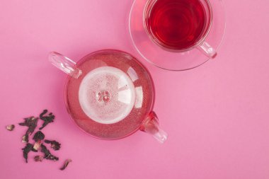 Cam çaydanlıkta Hibiscus veya Karkade çayı ve pembe arka planda cam bardak. Üst Manzara. Boşluğu kopyala.