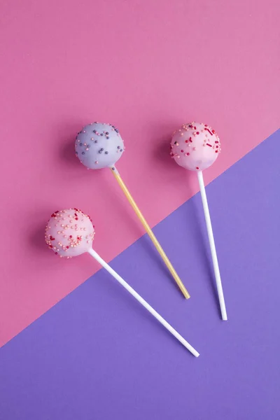 Cake pops with pink and violet glaze  on the two-color background. Top view. Copy space. Location vertical.