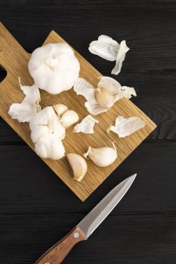 Siyah ahşap arka plandaki kahverengi kesme tahtasındaki kuru sarımsak. Üst Manzara. Uzayı kopyala Konum dikey.