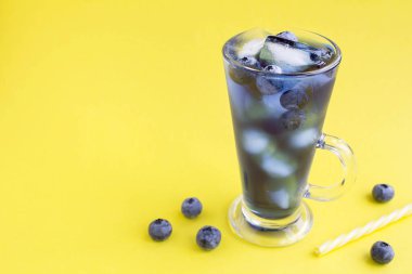 Glass of blue cocktail drink with ice and blueberry on the yellow  background. Copy space.