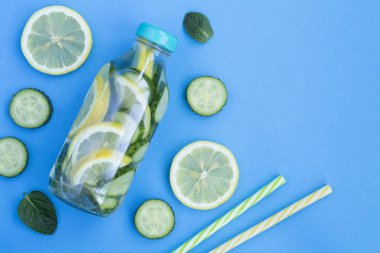 Mavi arka plandaki cam şişede limon, salatalık ve nane ile detoks ya da aşılanmış su. Üst Manzara. Boşluğu kopyala.