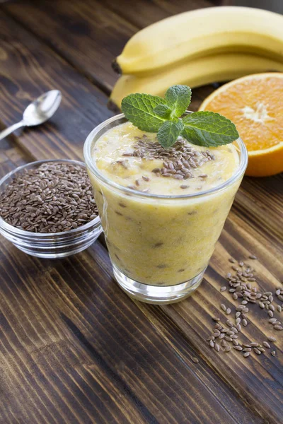 Smoothies with flax seeds, orange and banana  in the glass on the brown wooden  background. Location vertical.