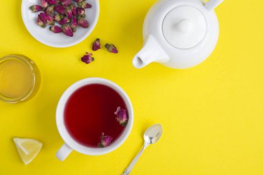 Sarı arka planda beyaz fincanda pembe güller olan bitkisel çay. Üst Manzara. Boşluğu kopyala.