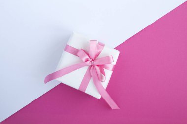 İki renkli arka planda pembe fiyonklu bir hediye. Üst Manzara. Boşluğu kopyala.
