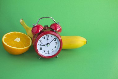 Kırmızı alarm saati, muz ve turuncu karışımı yeşil arka planda. Uzayı kopyala Yakın çekim..