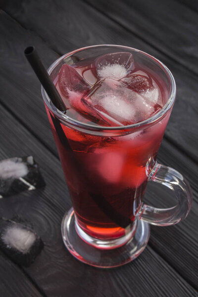 Iced hibiscus or karkade tea in the glass on the black wooden  background. Location vertical. Closeup.