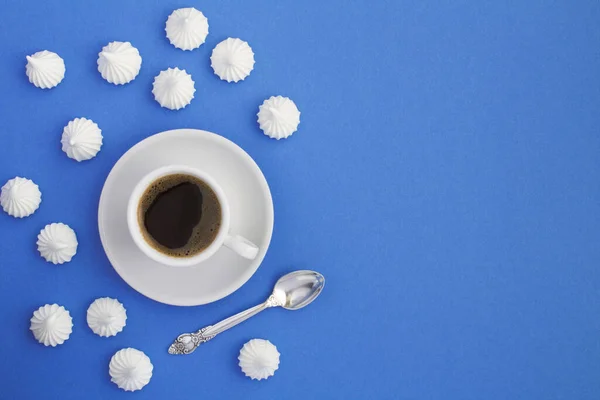 Black coffee in the white cup  and white meringue on the blue background. Top view. Copy space.