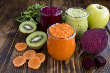 Kahverengi ahşap arka plandaki küçük cam kavanozlarda farklı sebze ve meyve püresi ya da püresi. Yakın çekim..