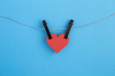 Mavi arka planda gri ipte siyah mandallı kırmızı bir kalp. Boşluğu kopyala.