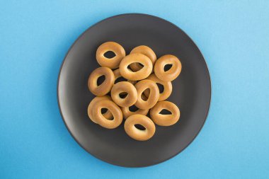 Mavi arka planda, siyah bir tabakta simit. Üst Manzara. Yakın çekim..