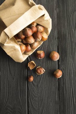 Siyah ahşap arka planda kağıt torbada fındık. Konum dikey. Görmek için. Boşluğu kopyala.
