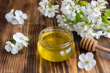 Cam kavanozdaki bal ve kahverengi ahşap arka plandaki beyaz çiçek açan ağaç dalları. Yakın çekim..
