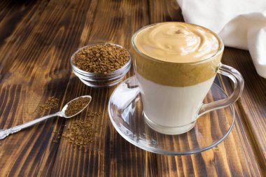 Kahverengi ahşap arka plandaki cam fincanda Dalgona kahvesi. Yakın çekim..