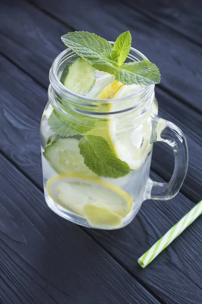 Sassy  water  slimming or infused water with lemon, cucumber and ginger in the glass on the black wooden  background. Location vertical.