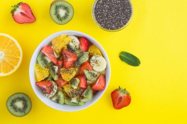 Sarı arka planda beyaz kasede chia tohumlu meyve salatası. Üst Manzara. Boşluğu kopyala.