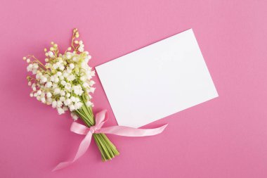 Boş beyaz kağıt ve pembe arka planda vadi zambakları. Üst Manzara. Boşluğu kopyala.