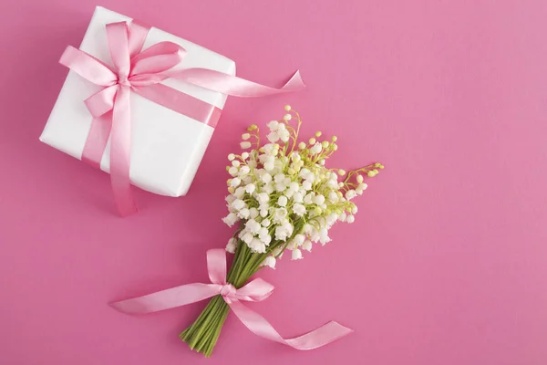 Bouquet of lilies of the valley  with pink bow and white gift box on the pink  background. Top view. Copy space.